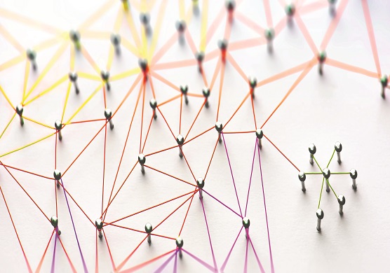Linking entities. Networking, social media, SNS, internet communication abstract. Small network connected to a larger network. Web of red, orange and yellow wires on white background. Shallow DOF. 